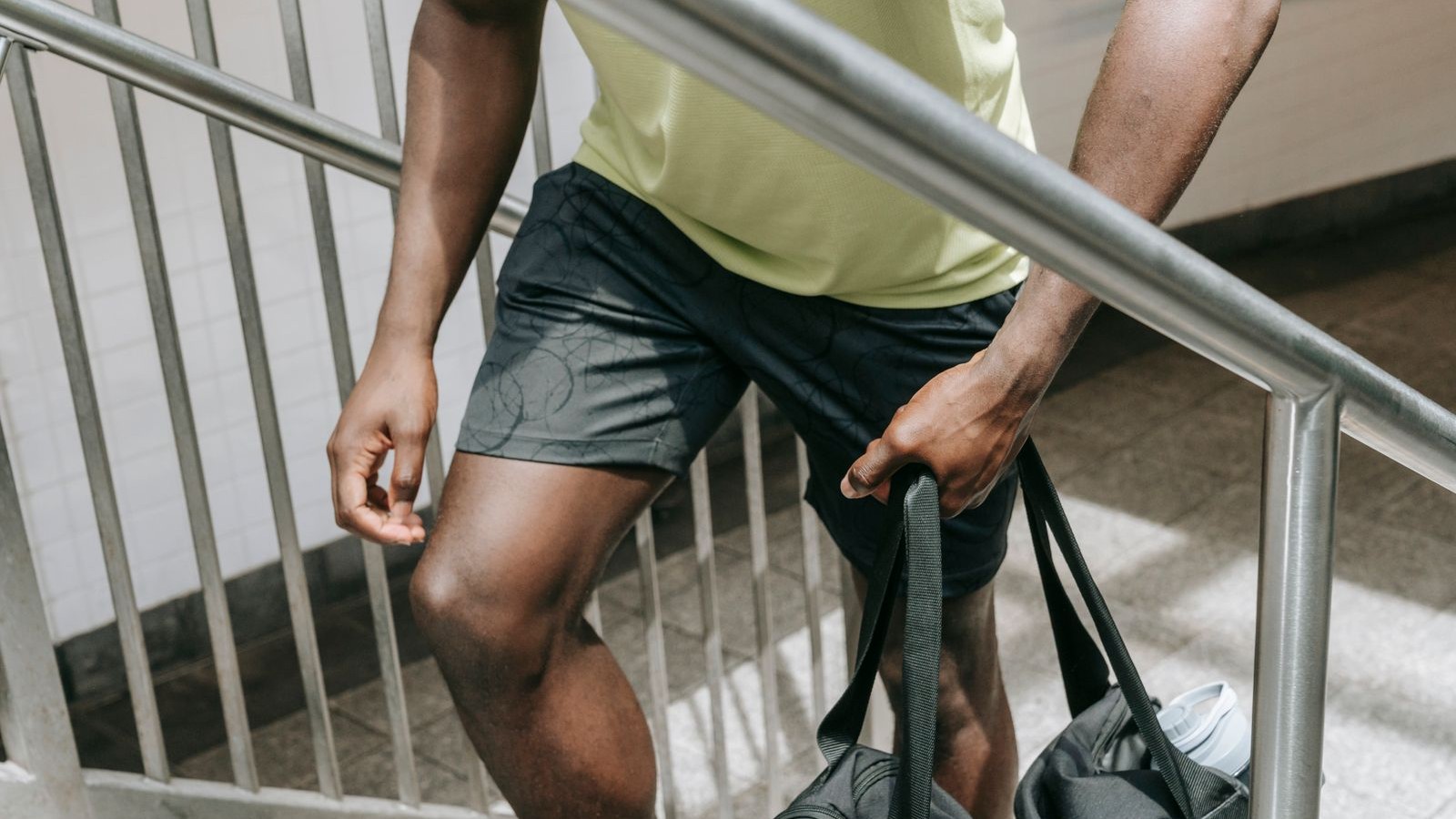 Person in athletic clothing carrying a gym bag up a stairway
