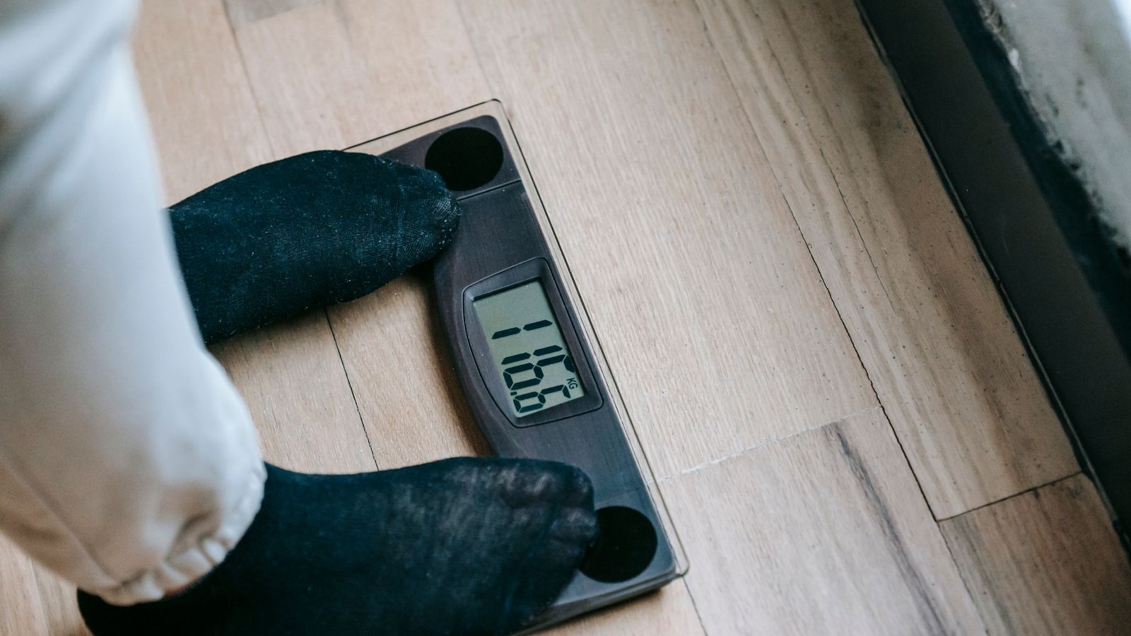 Person in socks stepping onto a digital bathroom scale on a wood floor