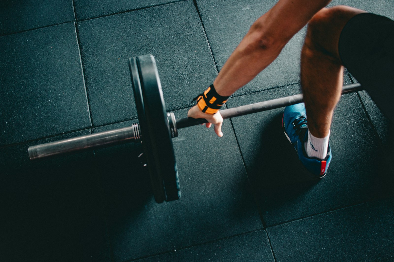 Close-up overhead shot of a man gripping a loaded barbell mid-deadlift on a gym floor
