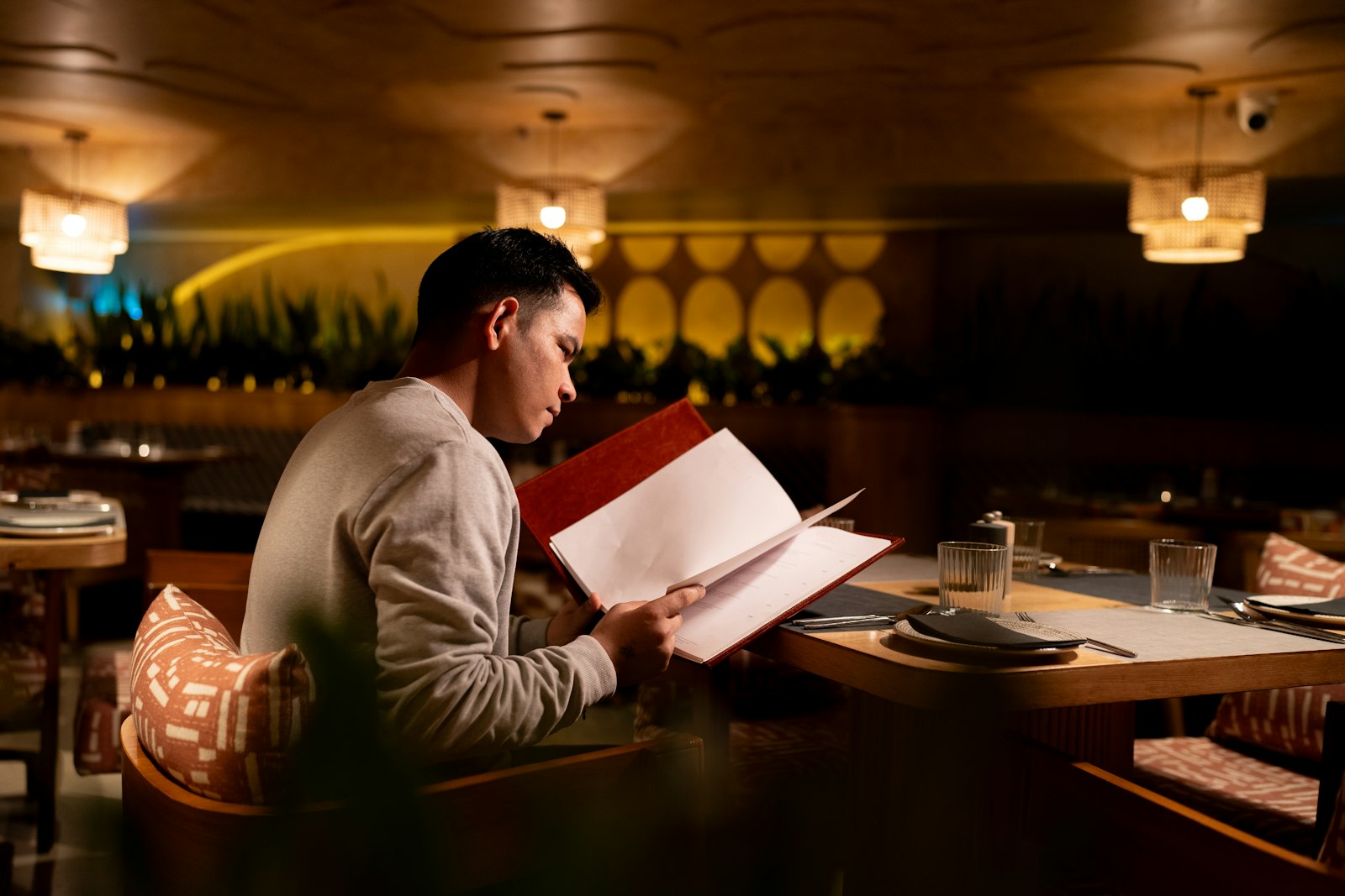 Man alone at a restaurant table at night, reading a menu under warm lighting
