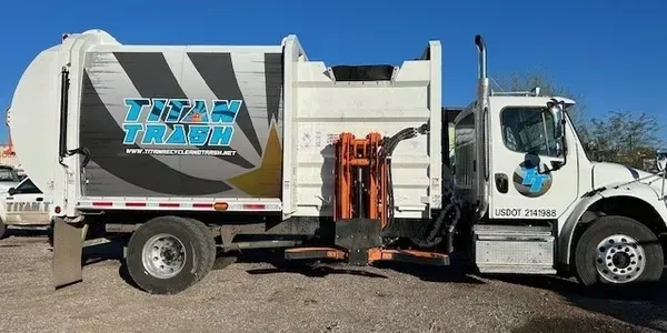 Four color-coded recycling bins labeled glass, metal, plastic, and paper lined up indoors beside a potted plant