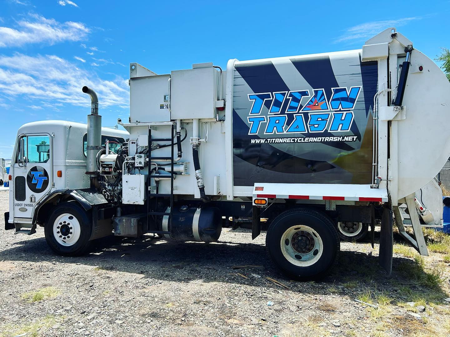Titan Trash garbage truck parked outdoors under a clear blue sky with company branding on the side.