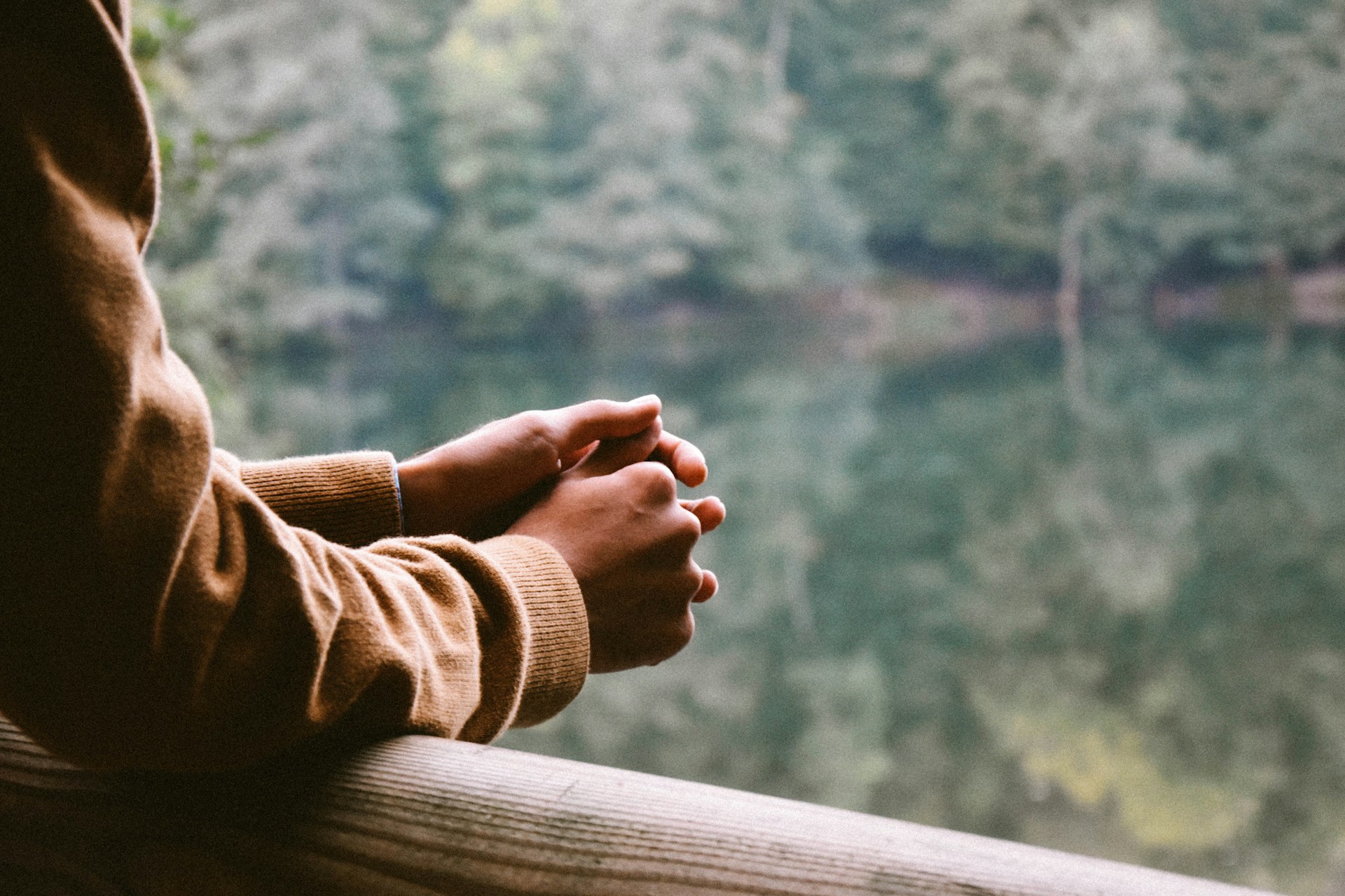 side view of a person leaning with their arms resting on a rail as they look out over a lake| Working With the Impact of Clinical Practice  Tempo Therapy and Consulting