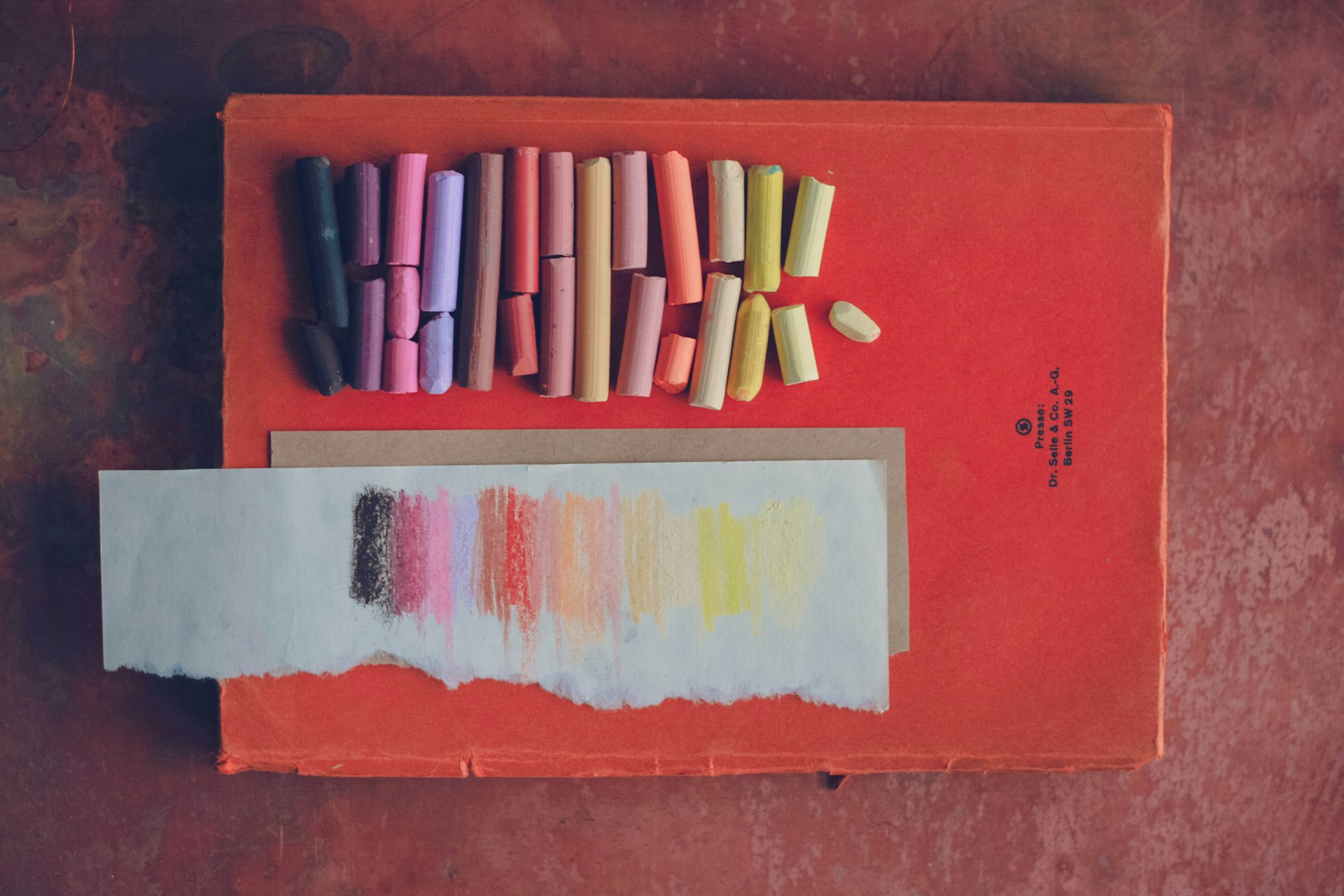 aerial view of warm coloured pastels lying on a burnt orange book and wooden table | Working With the Impact of Clinical Practice  Tempo Therapy and Consulting