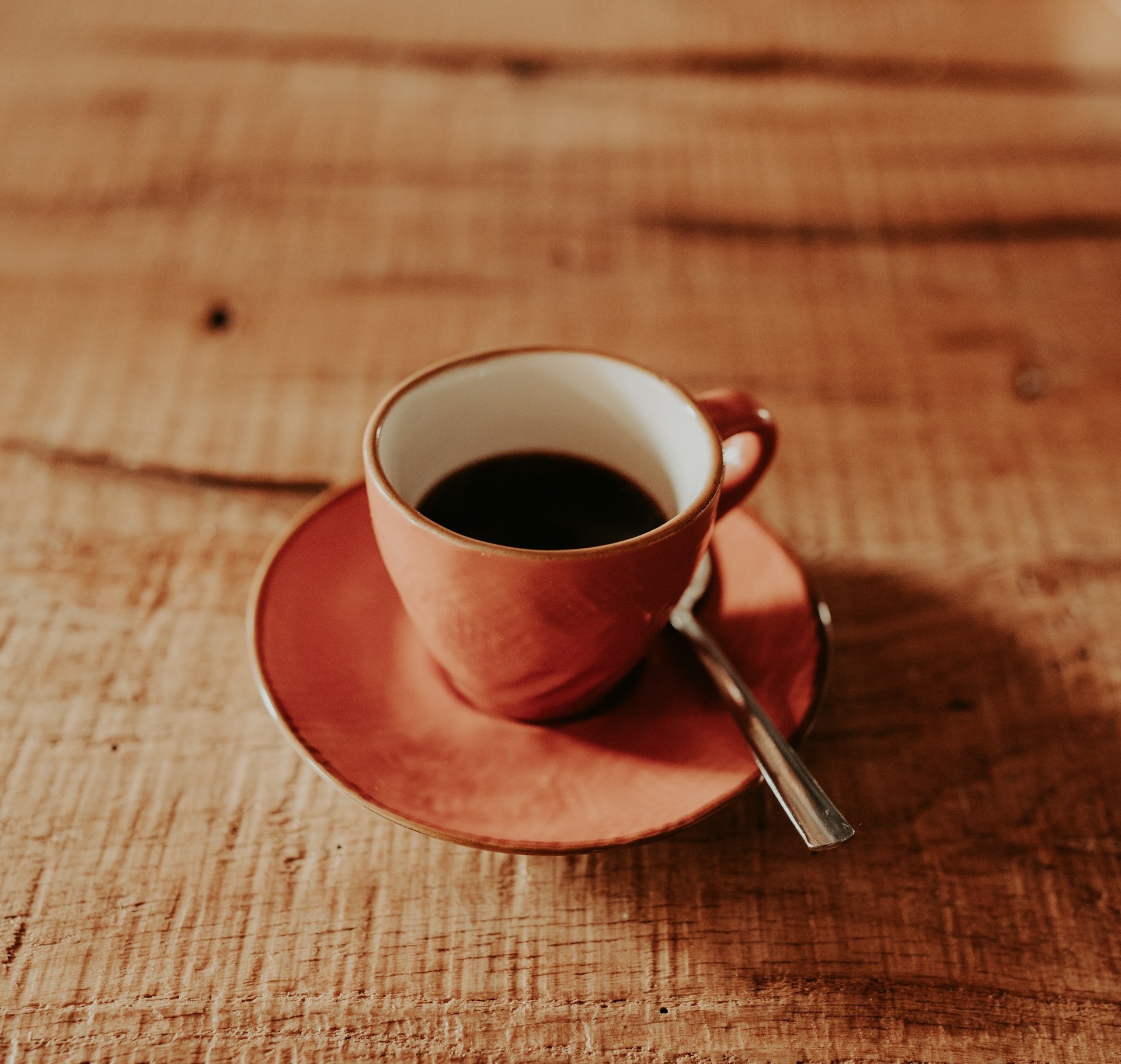 A pink ceramic cup on a warm timber bench in soft natural light
