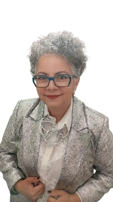 A middle-aged white woman with short blonde hair, wearing a tailored blue suit, standing confidently in front of a bookshelf filled with business books. The setting is warm and intellectual, suggesting expertise and approachability.