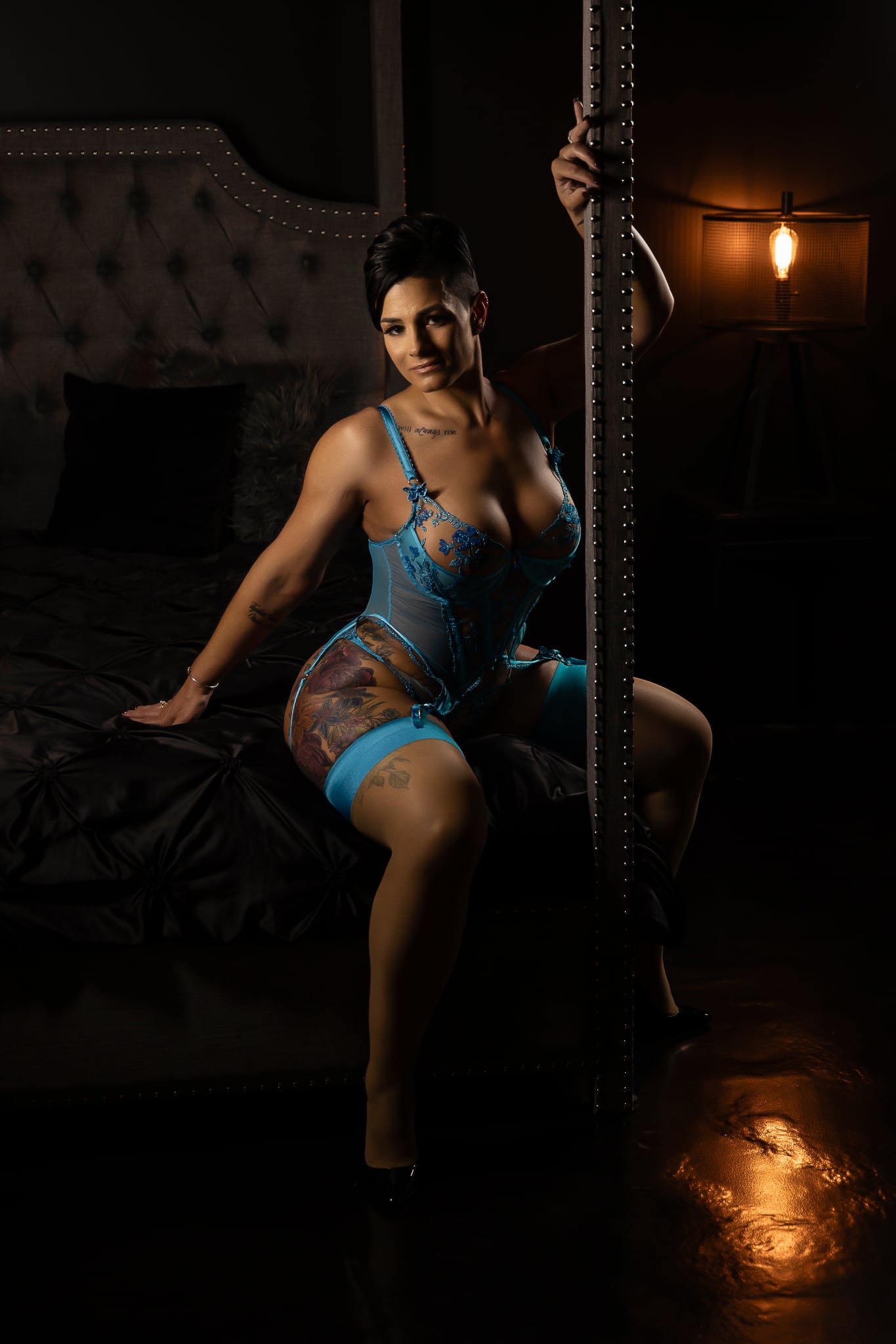 lady in teal lingerie and black heels sits on corner of bed in provocative pose