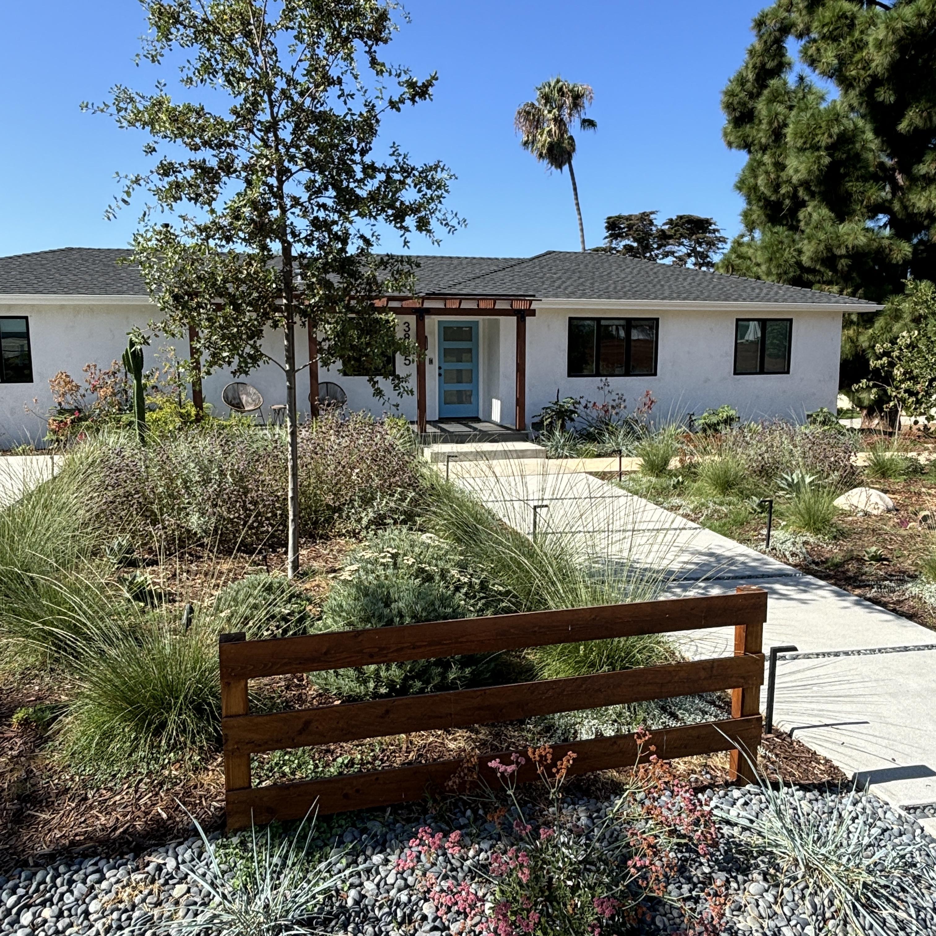 Front view of a white house with a bench and a lush grass garden.