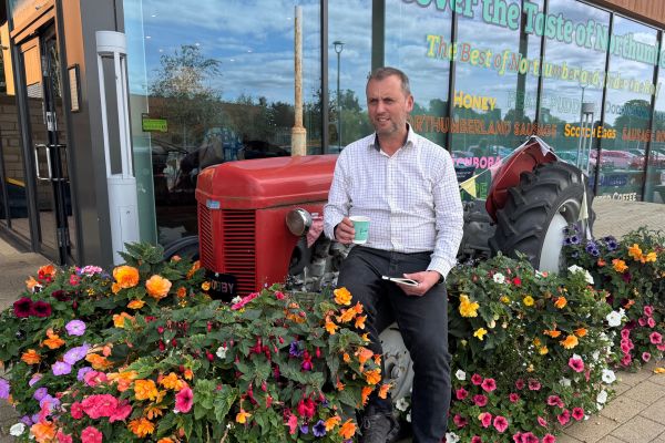 Mark enjoying some thinking time with a coffee and notebook, sitting on a tractor surrounded by flowers.