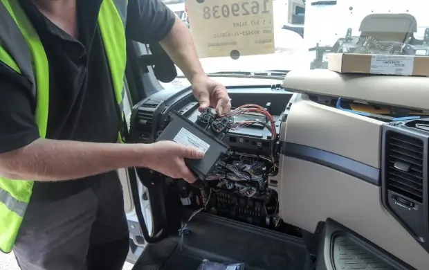 Fleet technician wiring and installing a GPS tracker into a truck dashboard as part of a custom telematics integration.