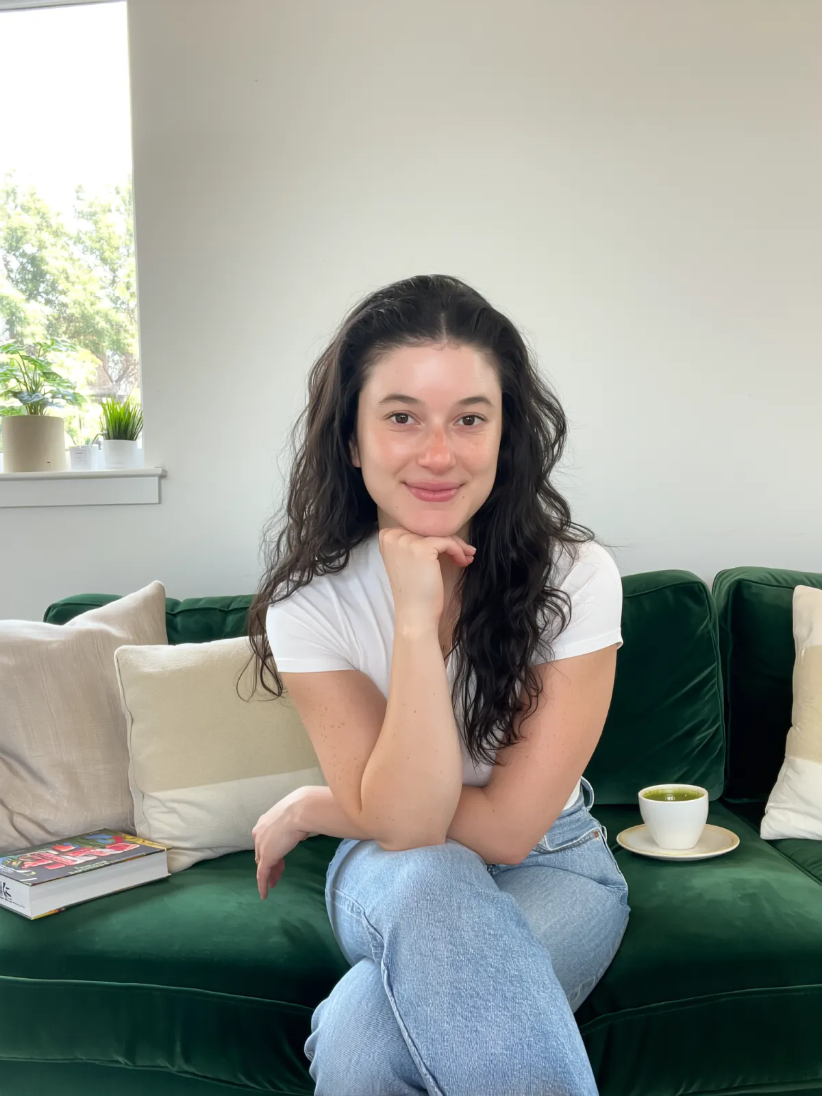 Barbara Guimarães sitting outside a café in a denim jacket, holding a coffee cup and smiling while enjoying a relaxed morning.