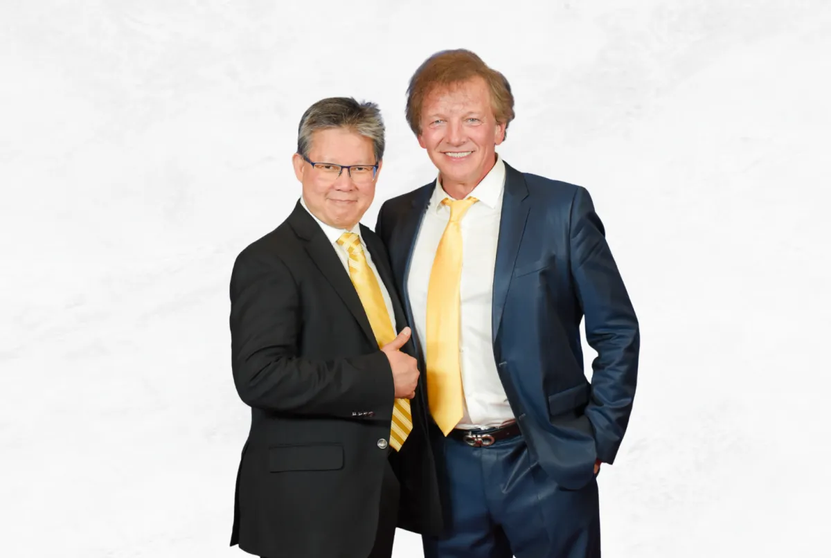 Sadikin Budiman standing with Andre Philippe, both smiling in business attire against a white background.