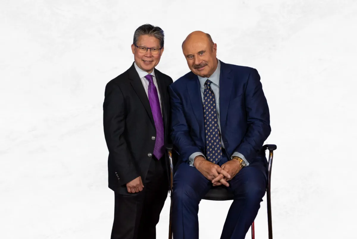 Sadikin Budiman standing with Dr. Phil in a studio portrait, both dressed in suits against a white background.