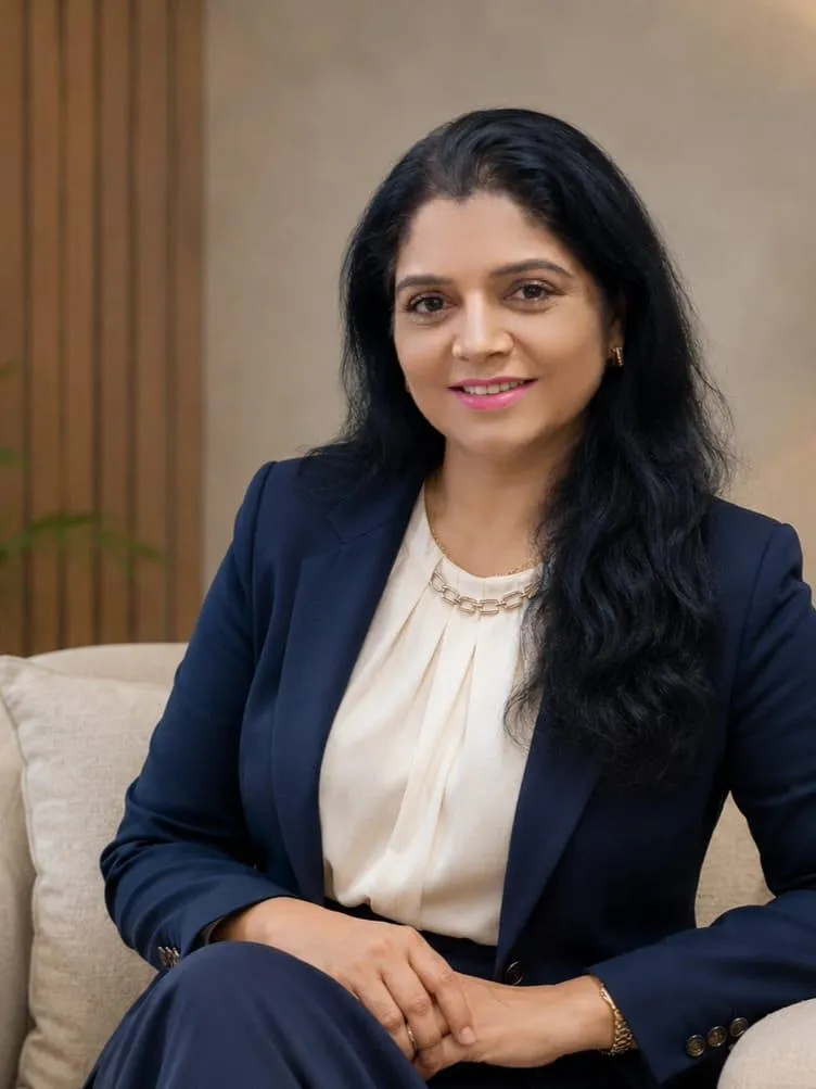 Professional head-and-shoulders portrait of an Indian woman in her thirties, smiling, in business clothing, against a LIGHT softly blurred background