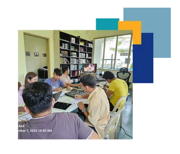 A group of people seated around a table in a room with bookshelves, engaged in a discussion or working on documents. A small screen in the background shows a video or presentation. The room has natural light coming in from large windows, and the timestamp on the bottom left corner reads 'September 7, 2023, 10:00 AM.