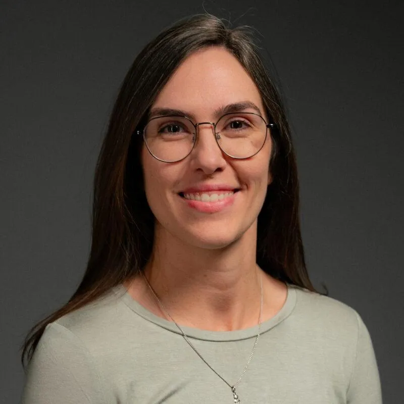 A portrait of a woman with long dark hair, wearing glasses with a smile.