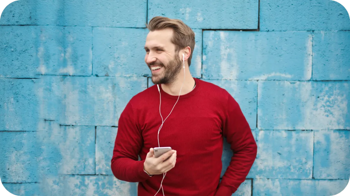 Man leaning against a blue wall with headphones in listening to a streaming app with music and advertisments