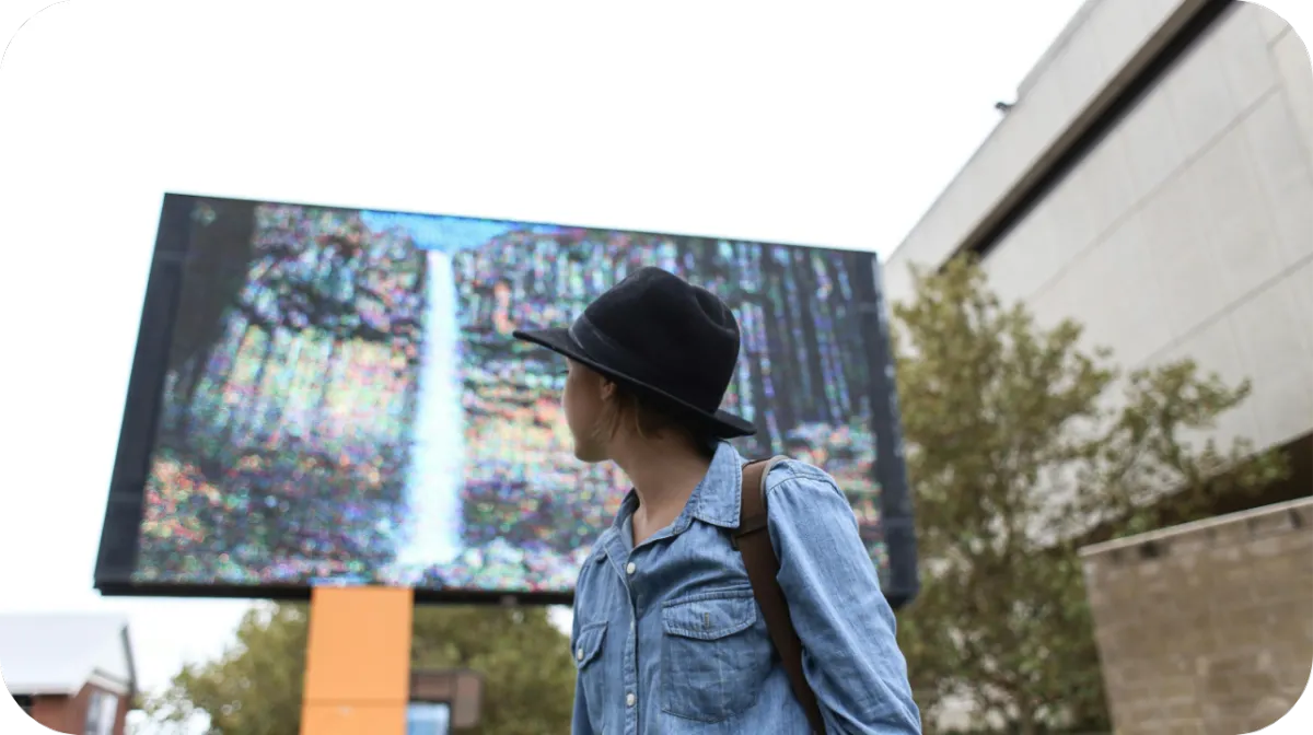 Person walking past a digital billboard that is serving them an image of the waterfall they have searched and want to visit