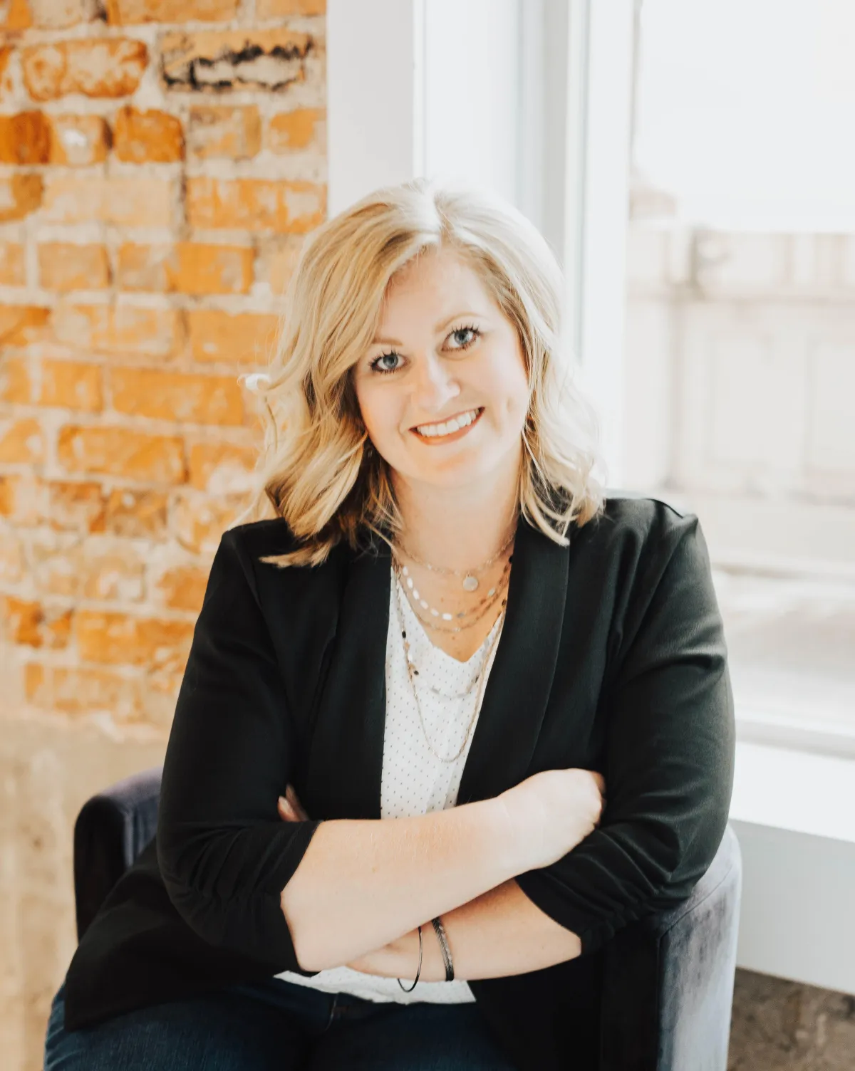 Professional headshot of Kristin Kippen, a smiling tax planning expert, sitting with her arms crossed in a modern office setting with an exposed brick wall background.