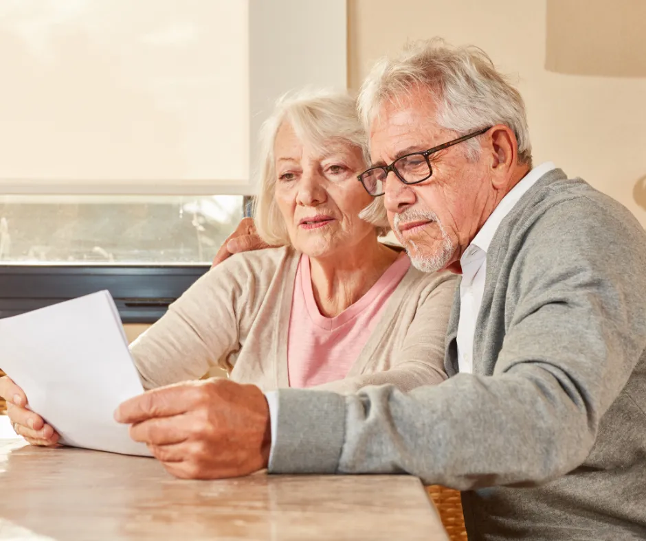 Elderly couple reviewing financial documents together at a table, looking focused and engaged.