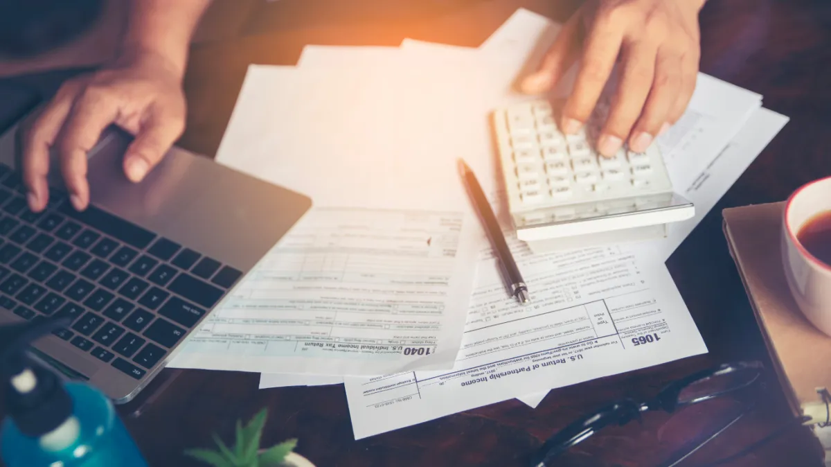 Close-up of a person using a calculator and laptop while working on tax forms, representing strategic tax planning and financial organization.