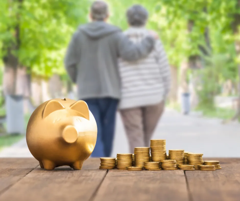 Golden piggy bank and stacked coins on a wooden surface with an elderly couple walking arm-in-arm in a blurred green park background, representing financial security and peace of mind in retirement.