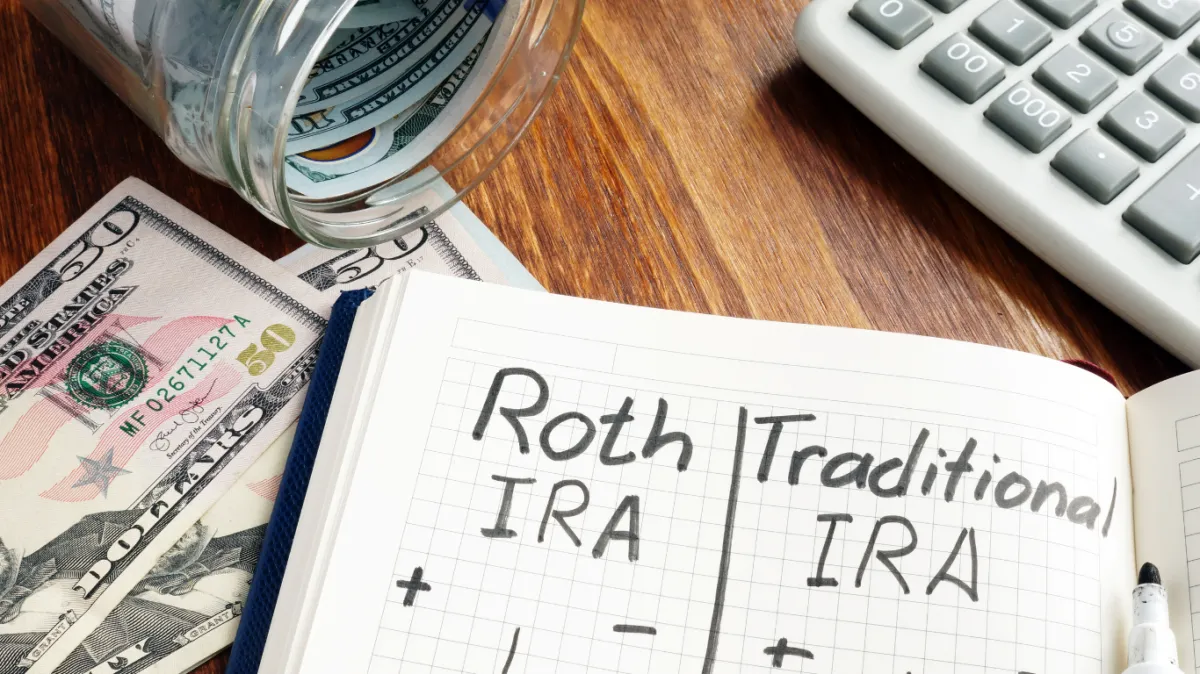 Comparison of Roth IRA and Traditional IRA in a notebook, surrounded by cash, a jar of savings, and a calculator, symbolizing retirement planning and financial decision-making.