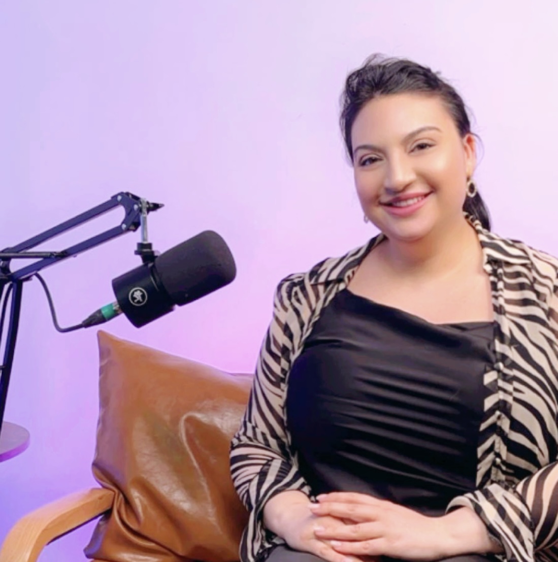 Anastasia sitting in a zebra jacket and black top smiling with a mic sticking out of the left pointing towards her.