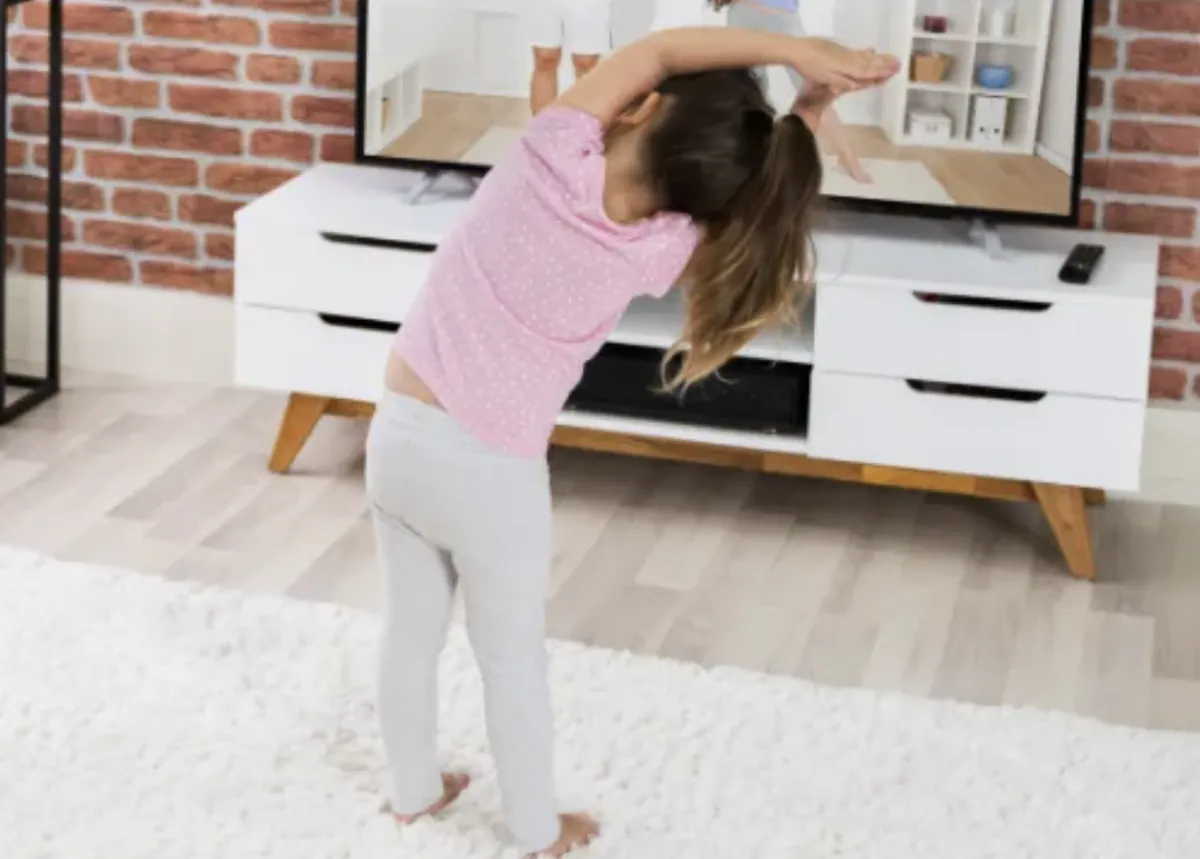 Girl stretches to the side while watching teacher on large screen TV