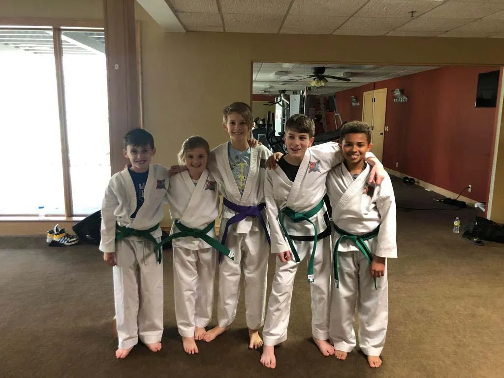 5 Ninja Fit karate students standing in uniform with arms around each other & smiling
