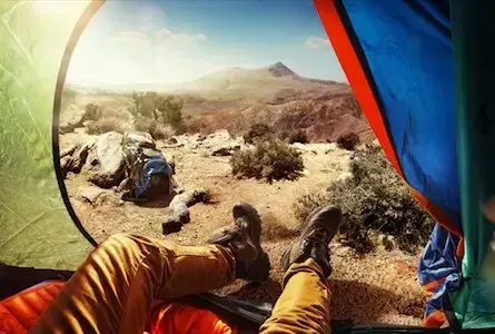 View from inside a tent showing a person’s legs in hiking boots and an arid landscape with mountains in the distance.