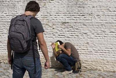 Teen bullying scene with the aggressor standing over his victim in a typical bullying scenario.