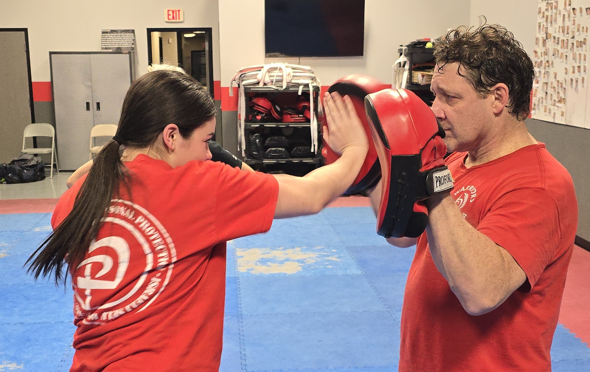 A picture of a teen girl student doing a palm heel strike into a focus mitt held by a coach