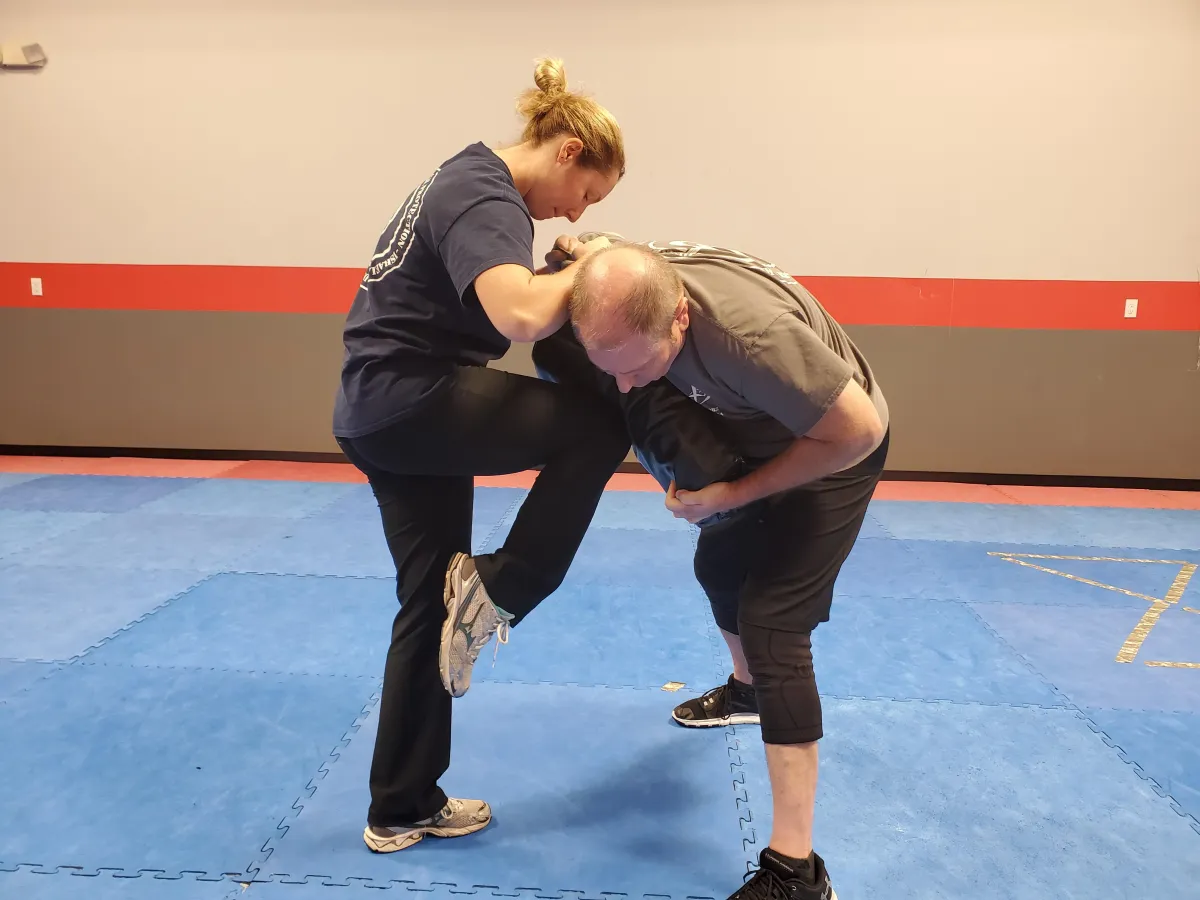 Female student training one-on-one at Krav Maga LKN, practicing knee strikes with an instructor.