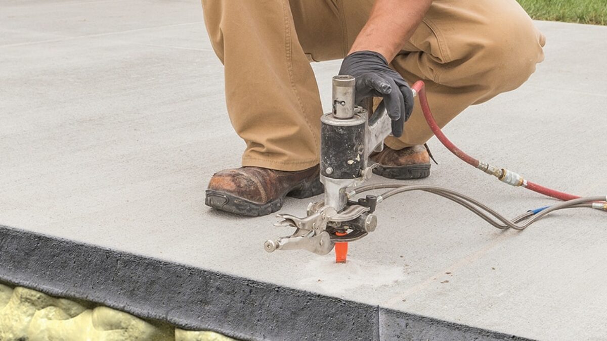 Worker applying polyurethane foam to lift and stabilize a sunken concrete slab.