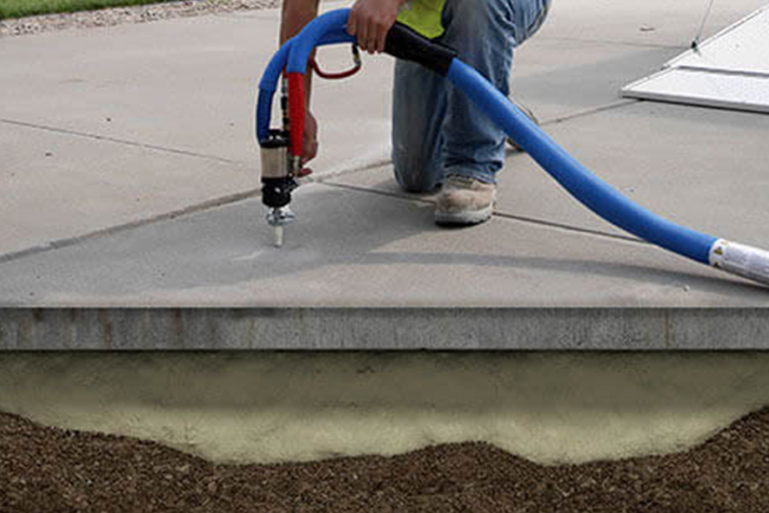 Worker injecting polyurethane foam beneath a sunken concrete slab during concrete leveling in Lansing, MI