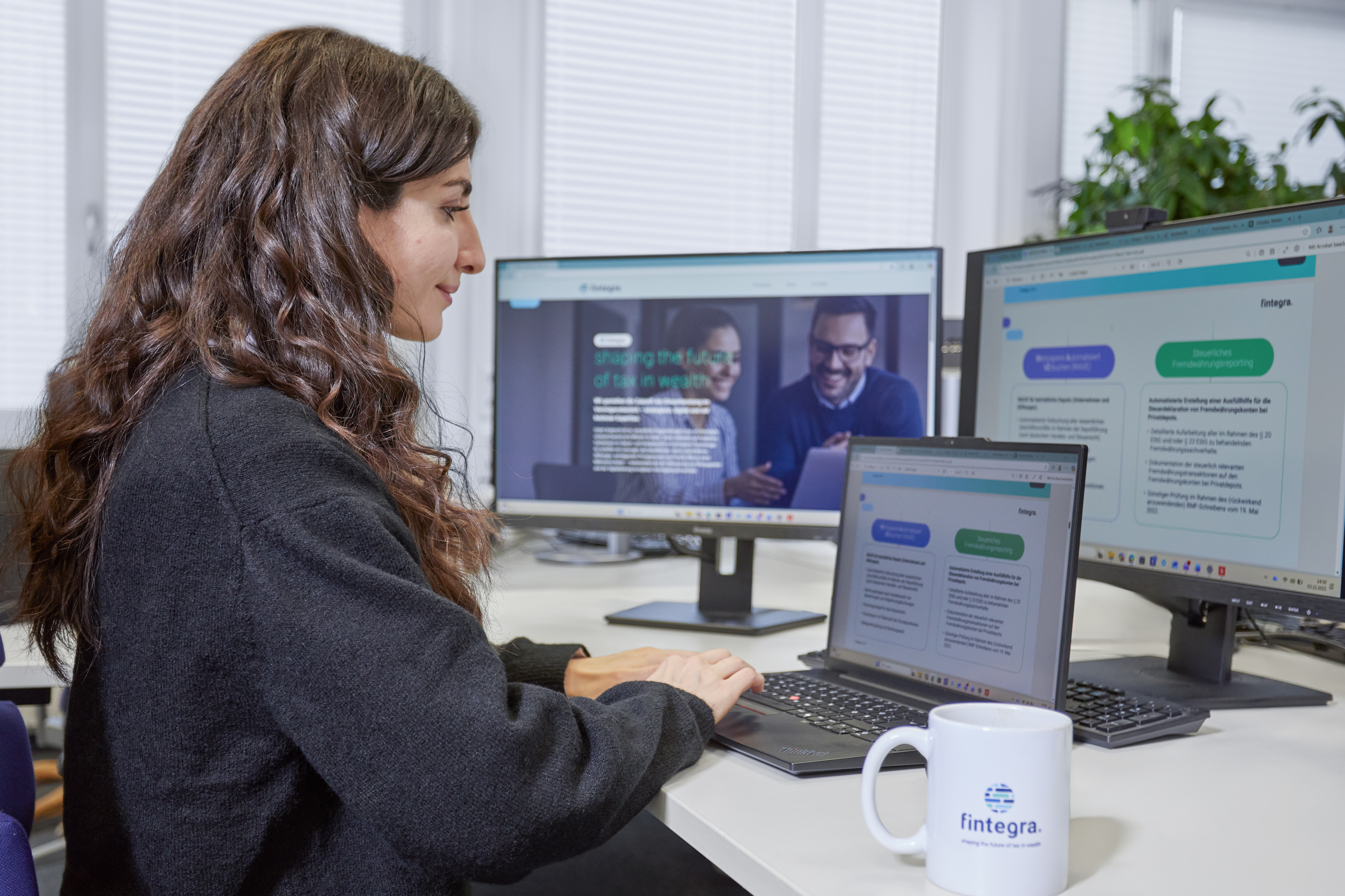 Mitarbeiterin arbeitet am Laptop und an mehreren Bildschirmen mit Software von fintegra