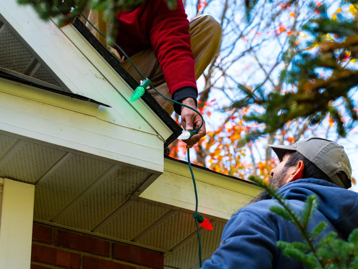 two men remove holiday lighting from a home