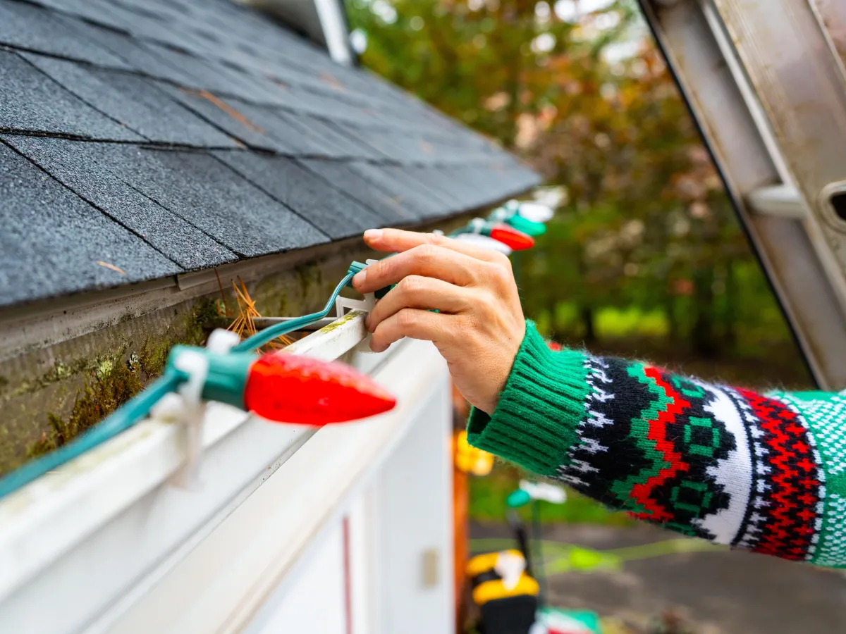 a hand tightens a holiday light on a home