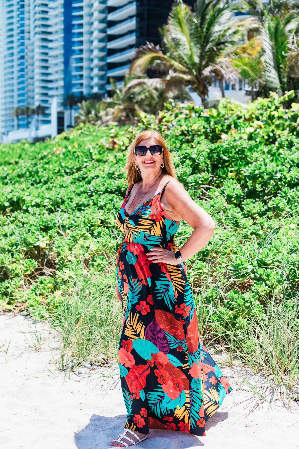 Image of Sandra on a recent business retreat she is standing on a sandy beach with shrubs behind her dressed in bright colours