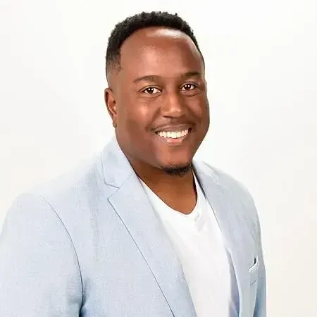 Troy Sandidge smiling in a light blue blazer and white shirt posing against a plain white background.