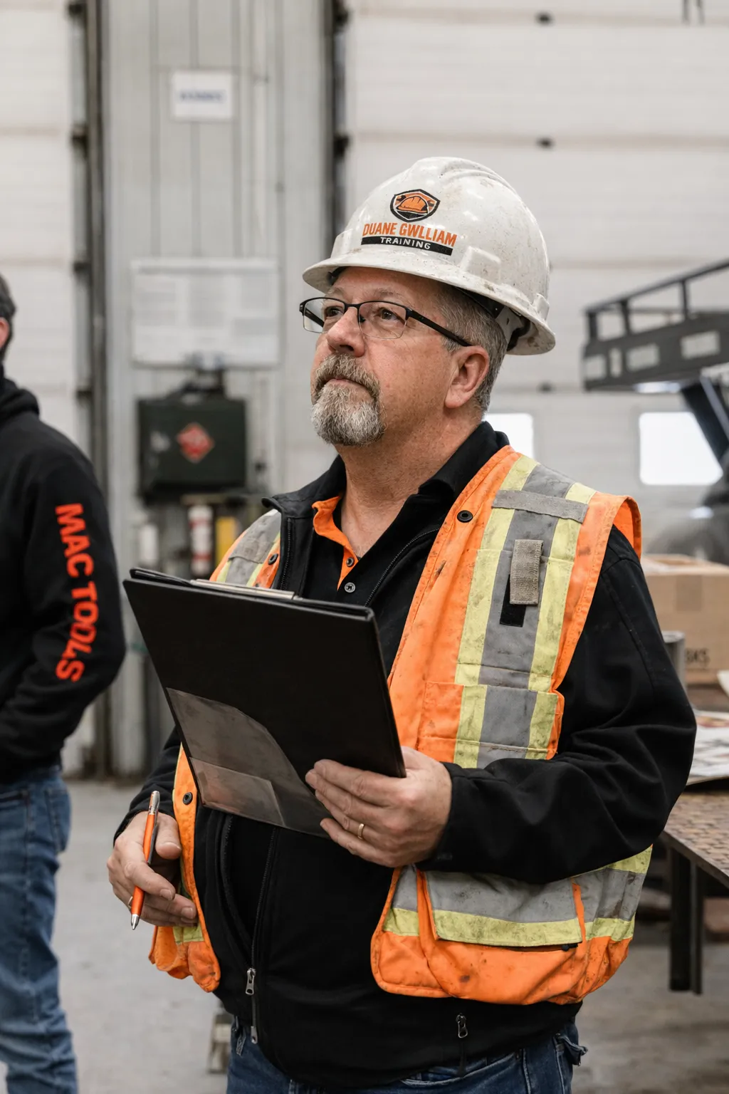 Vertical portrait of a trainer demonstrating a checklist on a tablet; clear subject with workshop attire, medium distance, natural light, not isolated — shows context and approachability.