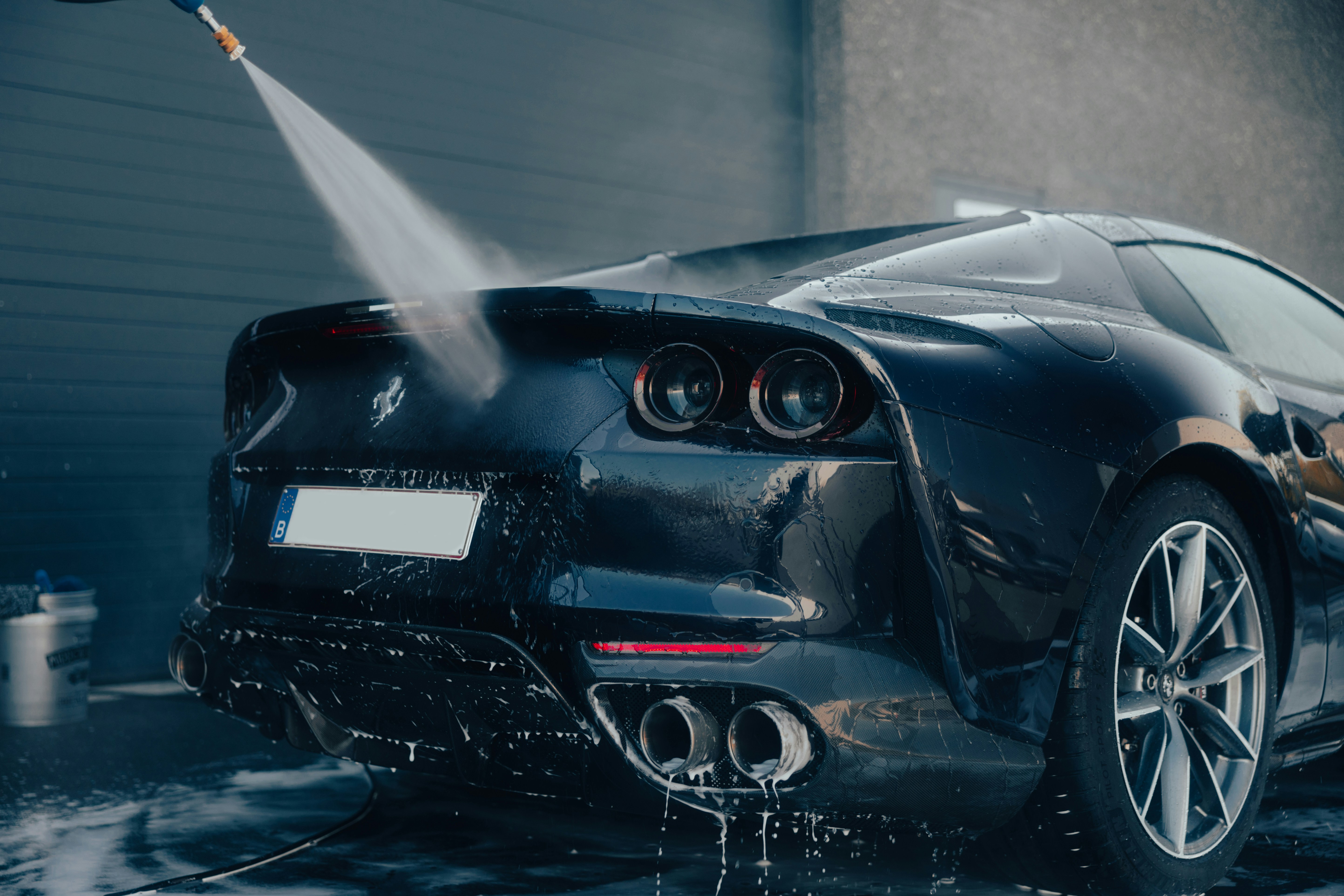 Image of the rear of a glossy black Ferrari being pressure washed.