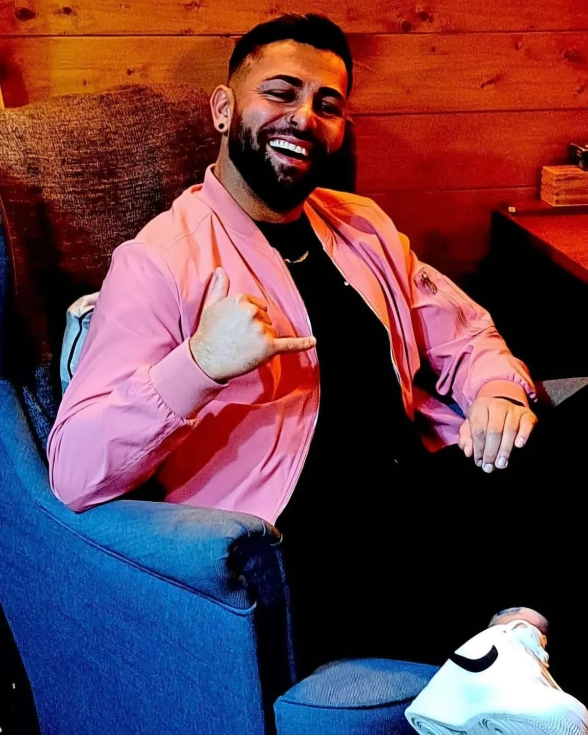 life coaching for confidence with Elaine Somerville, black haired asian manwearing black top nd jeans, with a pinkshirt, wood background and blue chair