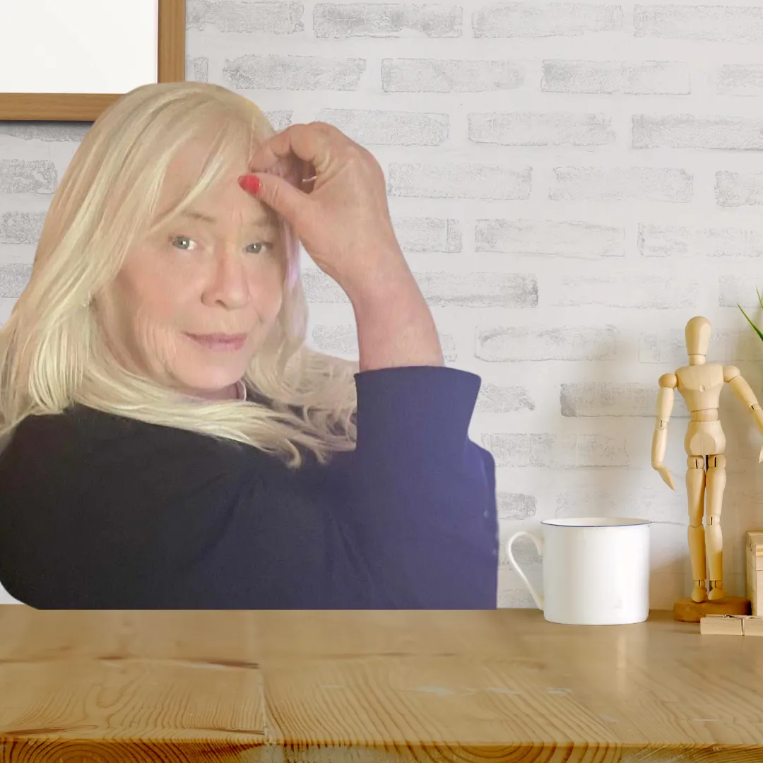 elaine somerville, blonde hair, red nails, blueeyes, nay lue hirt, siting at a wooden desk witha greybrick background, white coffee cup on the table with a wooden figure on the table