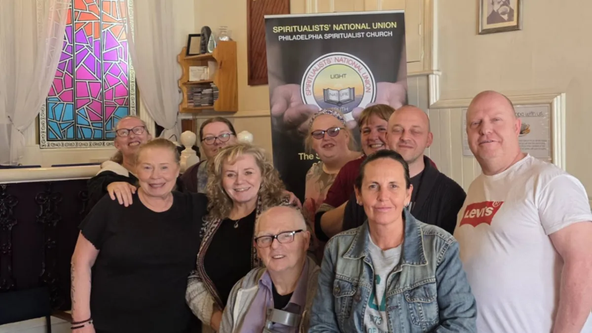 Students of Elaine Somerville, smiling, spiritualist national union banner, stained glass window in background