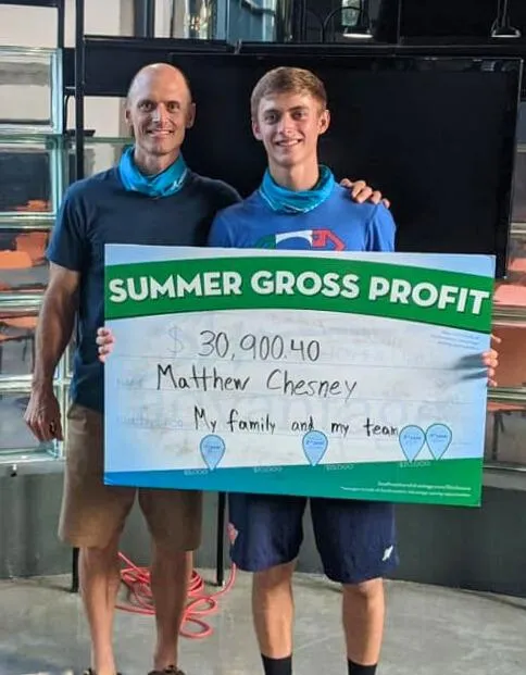 Infinite Banking Jake with his son Matthew Chesney holding a big check for a summer job