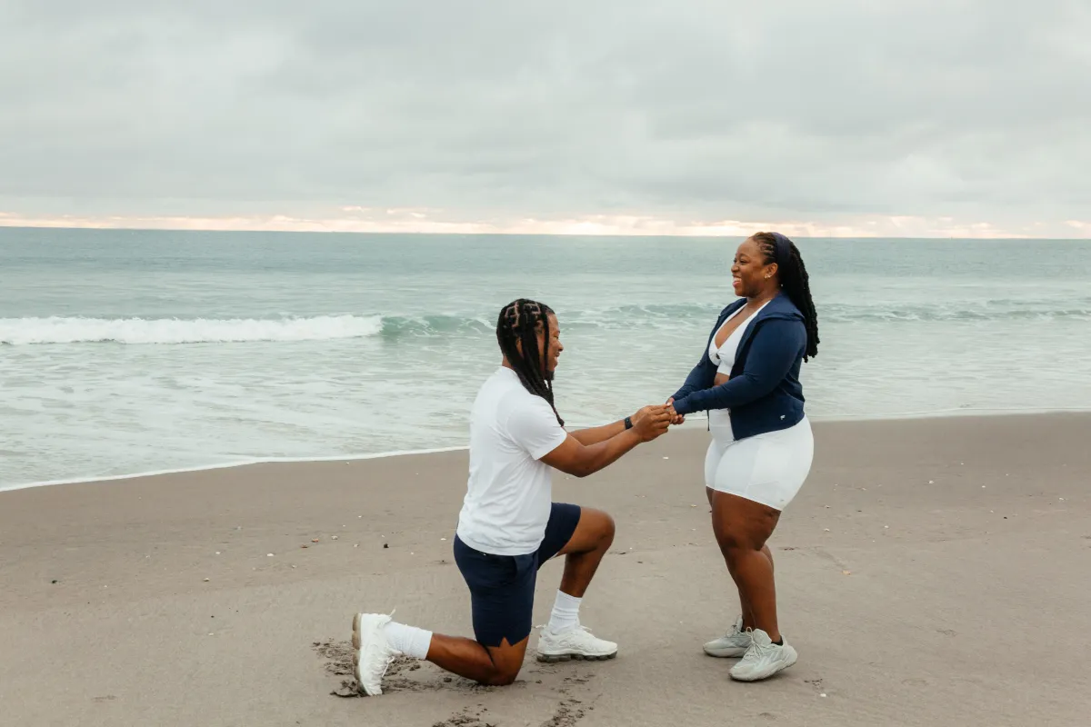 The groom's unexpected proposal and the bride's joyful reaction on a serene beach setting