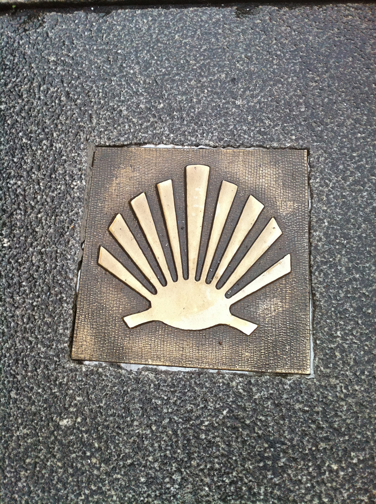 Scallop shell Camino marker set into dark stone pavement
