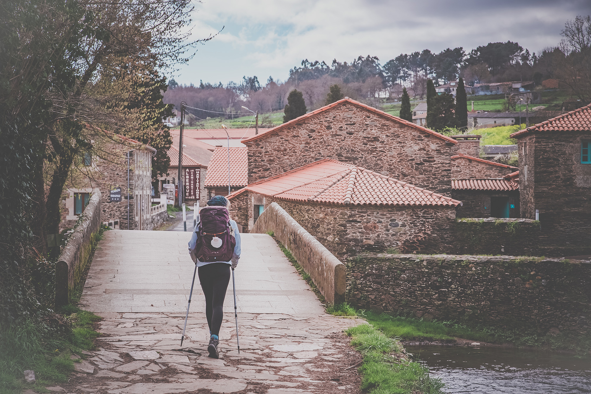 Pilgrim with walking poles crossing the medieval bridge at Ribadiso in Galicia